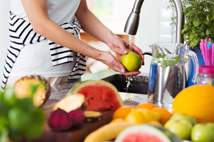 Healthy woman washing an apple above kitchen sink while preparing fresh breakfast with fruit