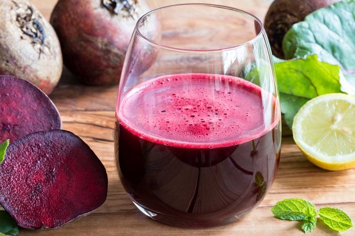 Red beet juice in a glass on a wooden background with lemon and beet greens